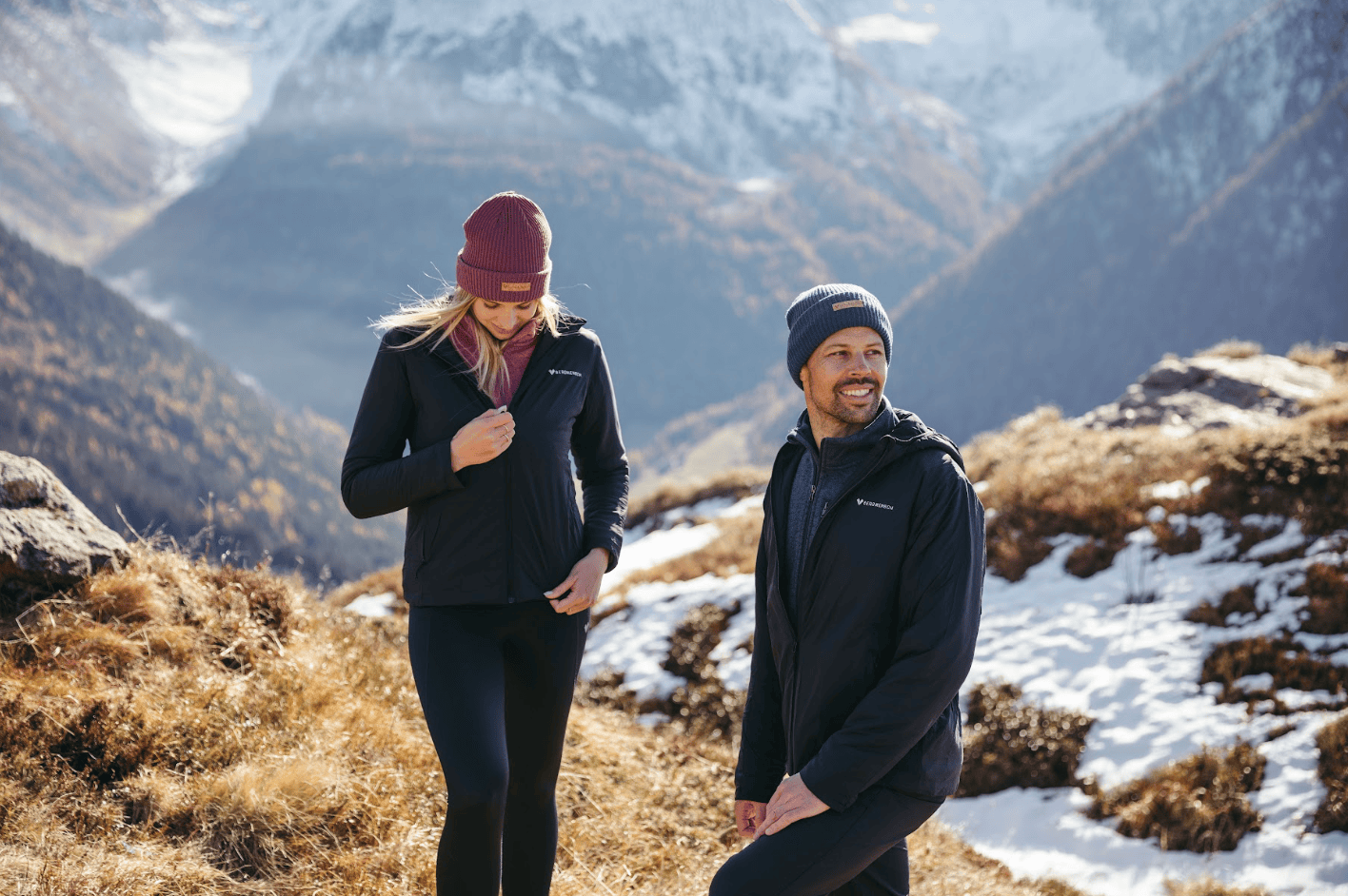 Models tragen schwarze Thermolite Jacken und Cozy Fleece Beanies von BERGMENSCH in den verschneiten Bergen