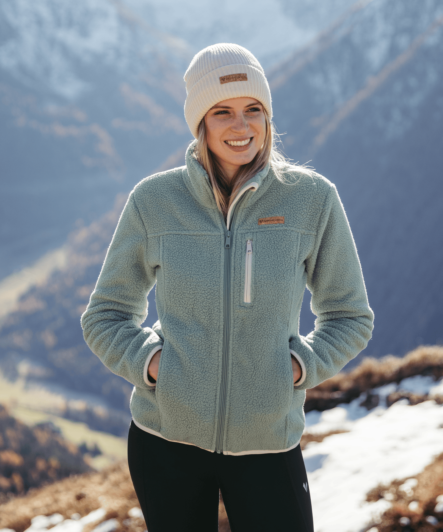 Model trägt die BERGMENSCH Damen Sherpa Fleece Jacke in der Farbe Sage und die Cozy Fleece Beanie in der Farbe Whitecap Grey