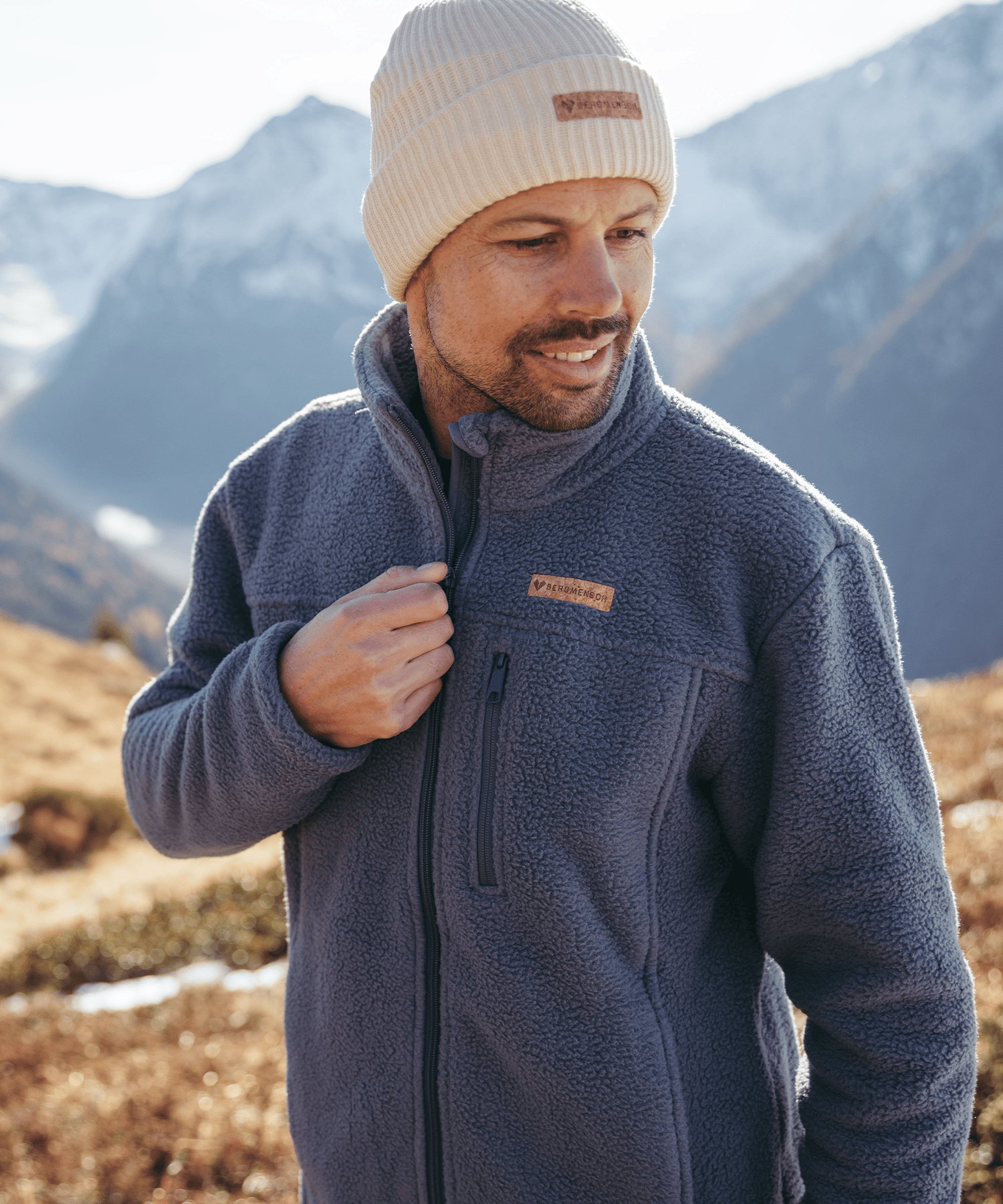 Model trägt die BERGMENSCH Herren Sherpa Fleece Jacke in der Farbe Stormy Weather und die Cozy Fleece Beanie in der Farbe Whitecap Grey