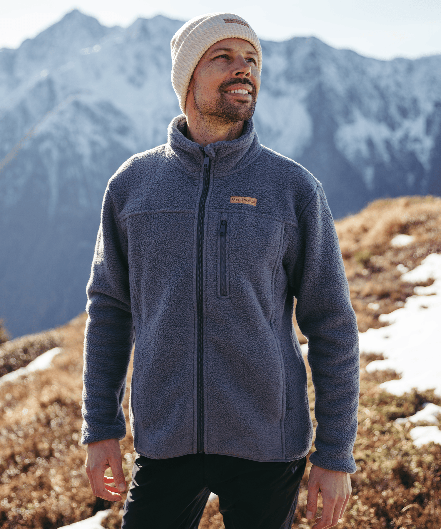 Model trägt die BERGMENSCH Herren Sherpa Fleece Jacke in der Farbe Stormy Weather und die Cozy Fleece Beanie in der Farbe Whitecap Grey